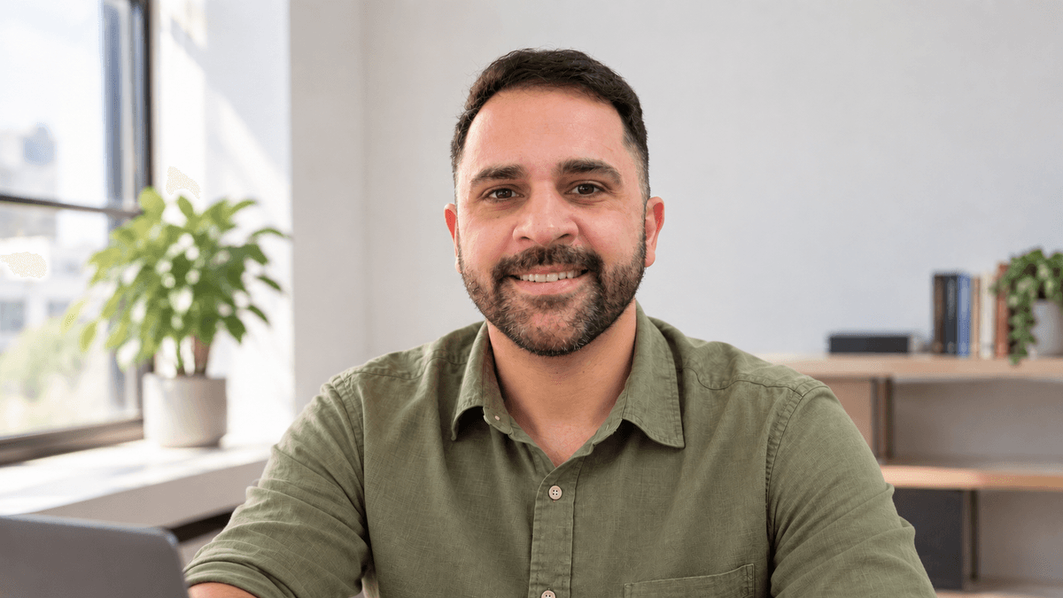 Retrato profissional de Juliano de camisa verde, sorrindo para a câmera num escritório claro