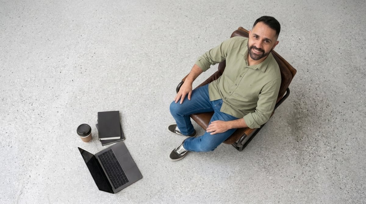 Juliano visto de cima, sentado com laptop, caderno e café num estúdio amplo e claro